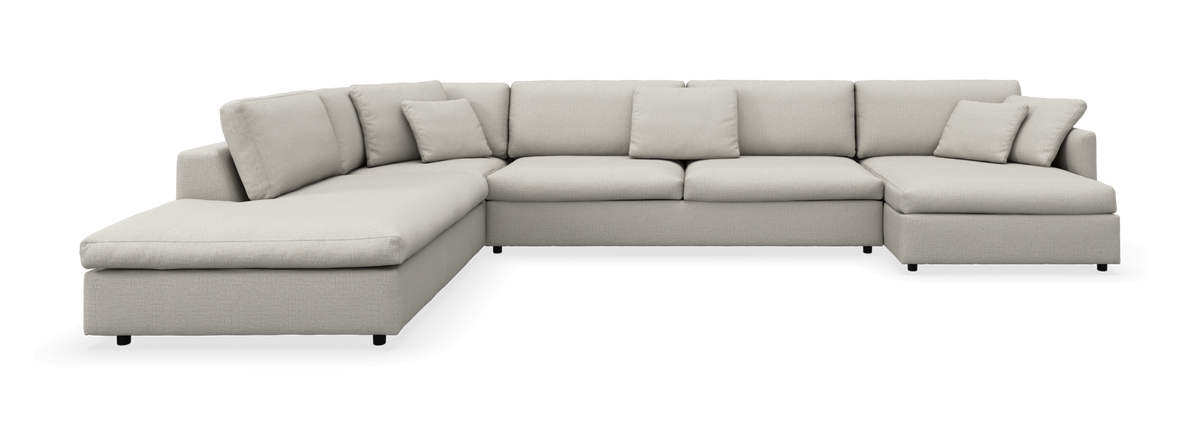 Lysebeige U-formet modulsofa med chaiselong i begge ender, løse ryghynder og små pyntepuder, frilagt mod neutral baggrund.