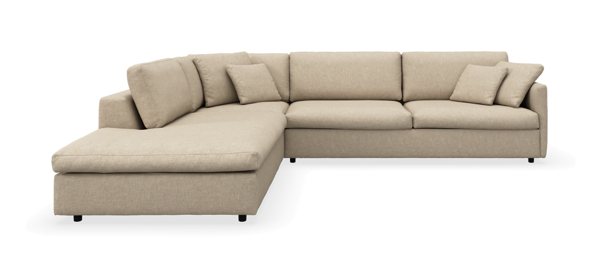 Beige L‑formet hjørnesofa med chaiselong og flere løse puder, frilagt på hvid baggrund.