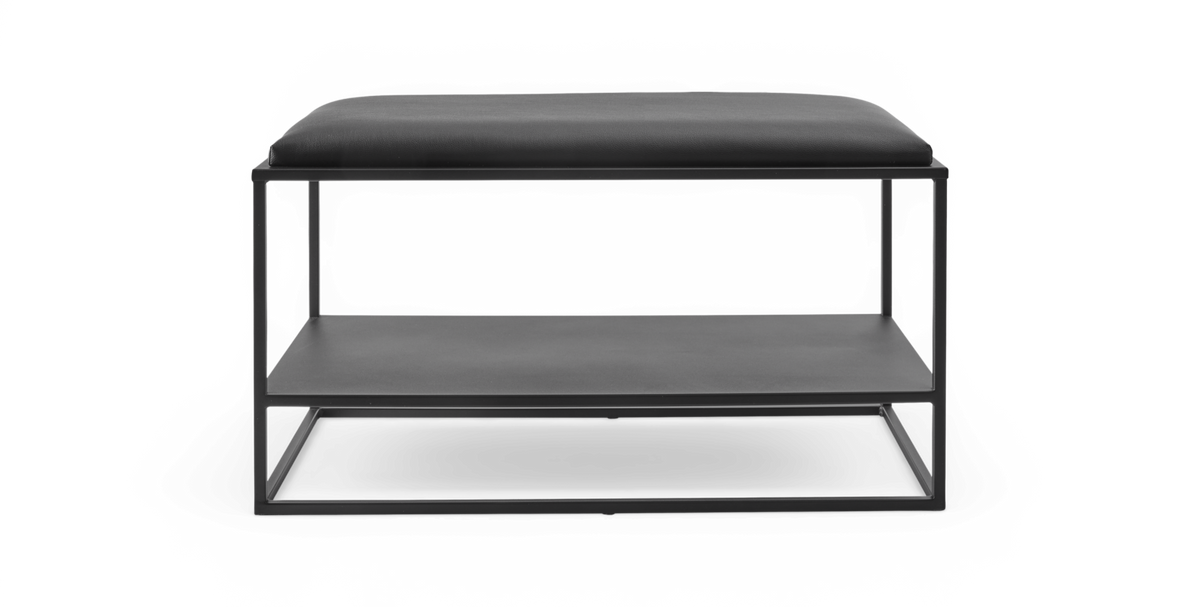 Sort minimalistisk bænk med polstret sæde og åben metalramme med hylde under, frilagt på hvid baggrund.
