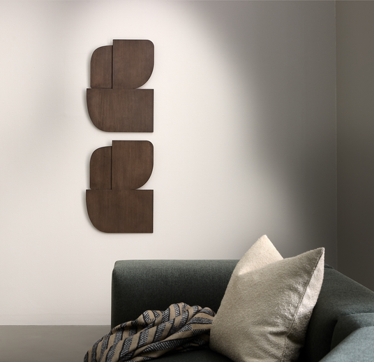 Minimalistisk stue med mørkegrøn sofa, beige pude og mønstret plaid; to vertikale geometriske trævægpaneler på en lys væg.