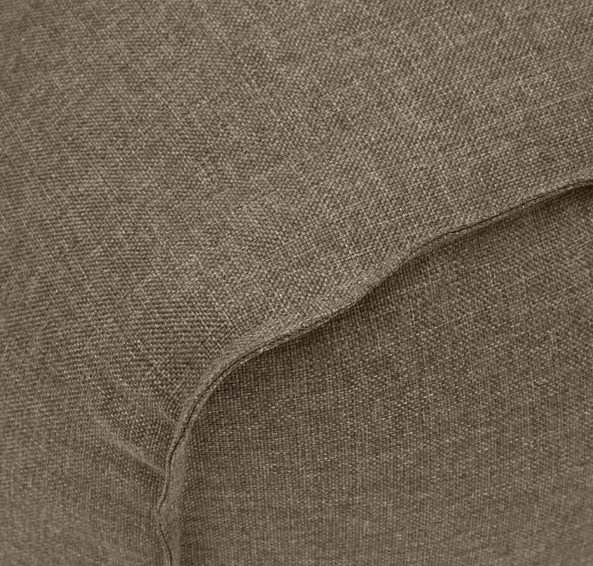 Nærbillede af brun-beige vævet tekstil med synlig søm på en polstret pude/sofa.
