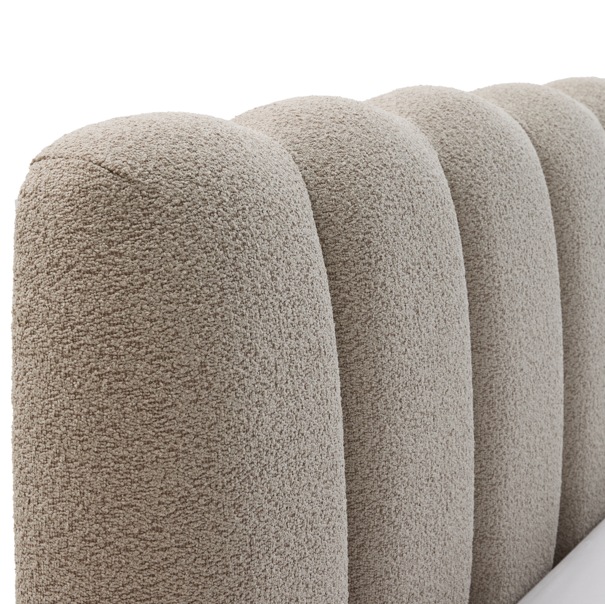 Nærbillede af rund, kanalpolstret sengegavl i beige bouclé.