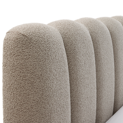 Nærbillede af rund, kanalpolstret sengegavl i beige bouclé.