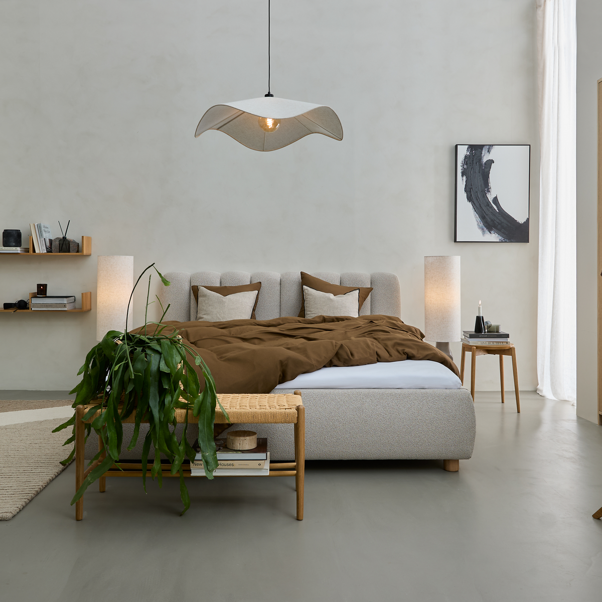 Roligt, minimalistisk soveværelse med polstret seng, brun dyne, træbænk med hængende grøn plante og bølgeformet pendel; blødt dagslys og abstrakt vægkunst.