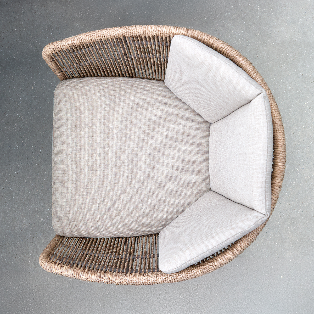 Set oppefra: rund loungestol med beige puder og flettet ryg i brun reb på gråt cementgulv.