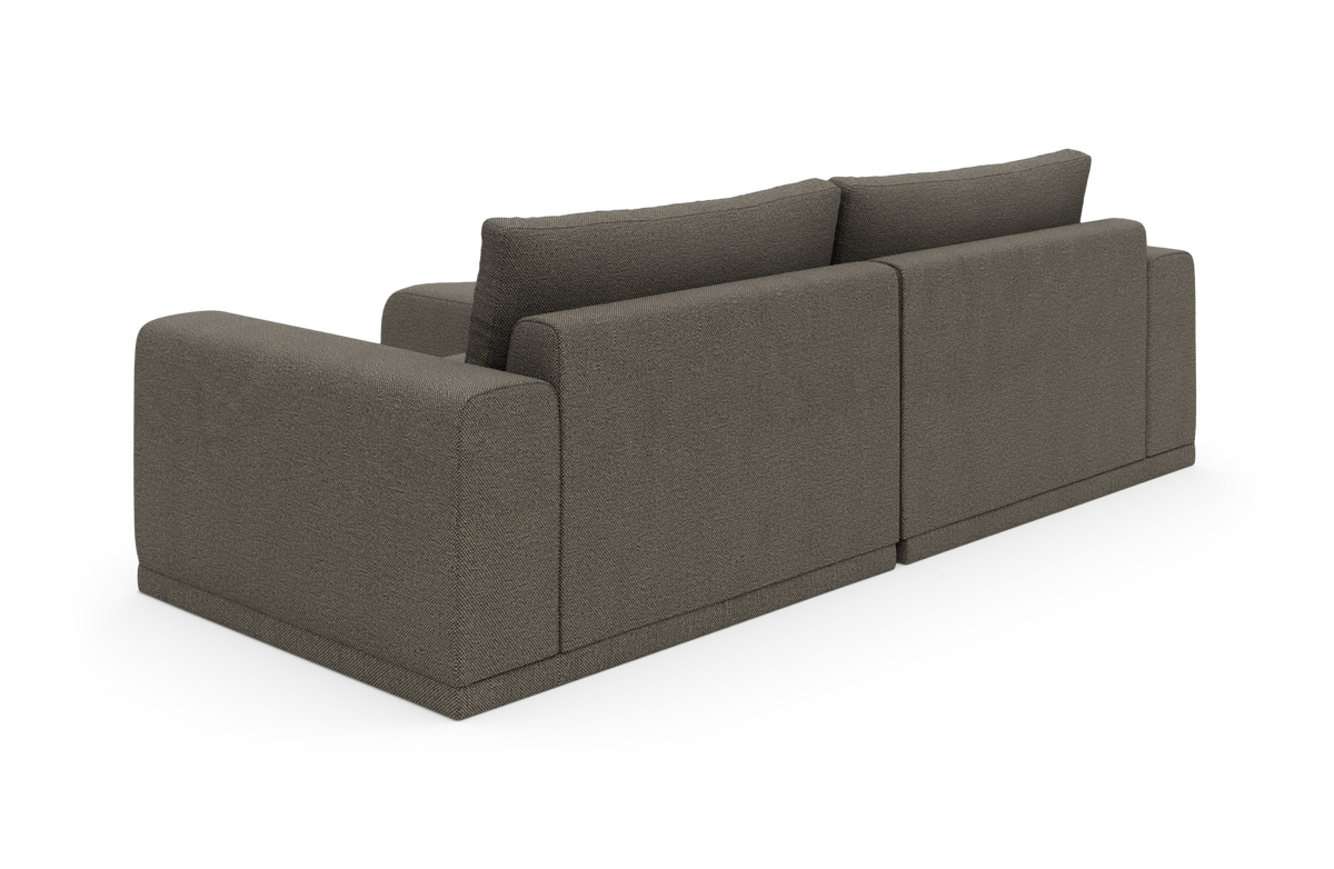 Mørkegrå modulsofa med brede armlæn set skråt bagfra i studie.