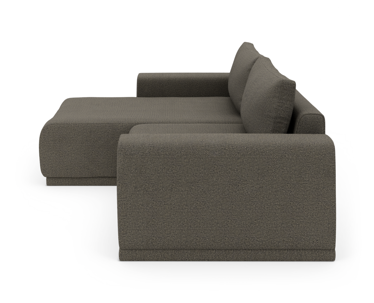 Sofa med chaiselong i mørkegråt stof, sidevinkel mod hvid baggrund.