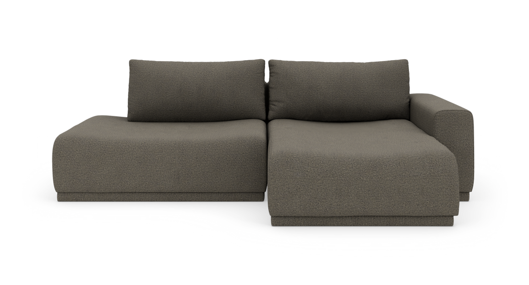 Modulsofa i mørkegrå tekstil med venstre chaiselong og højre armlæn, fritstående på hvid baggrund.