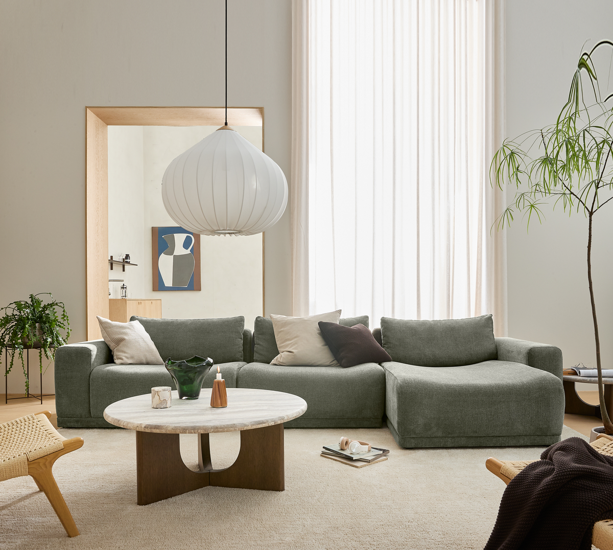 Lyst skandinavisk stue med grøn modulsofa, rundt marmorsofabord, stor hvid pendel, planter og lette gulvlange gardiner.