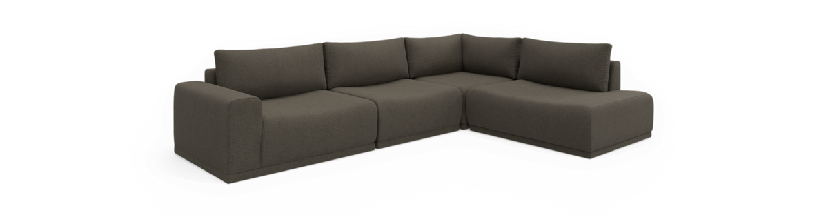 Mørkegrå L‑sofa i modulopbygning med chaiselong til højre, frilagt i studiemiljø.