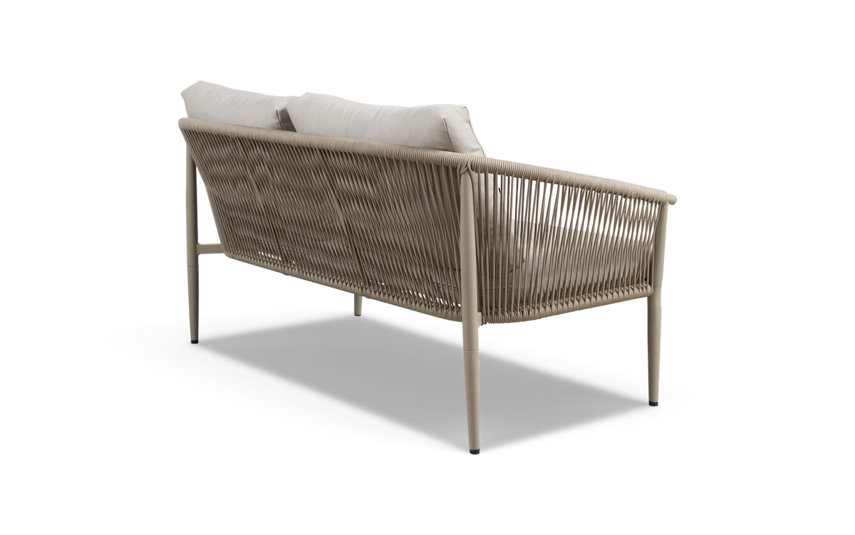 Udendørs sofa i beige reb med lyse puder, set skråt bagfra, fritlagt på hvid baggrund.