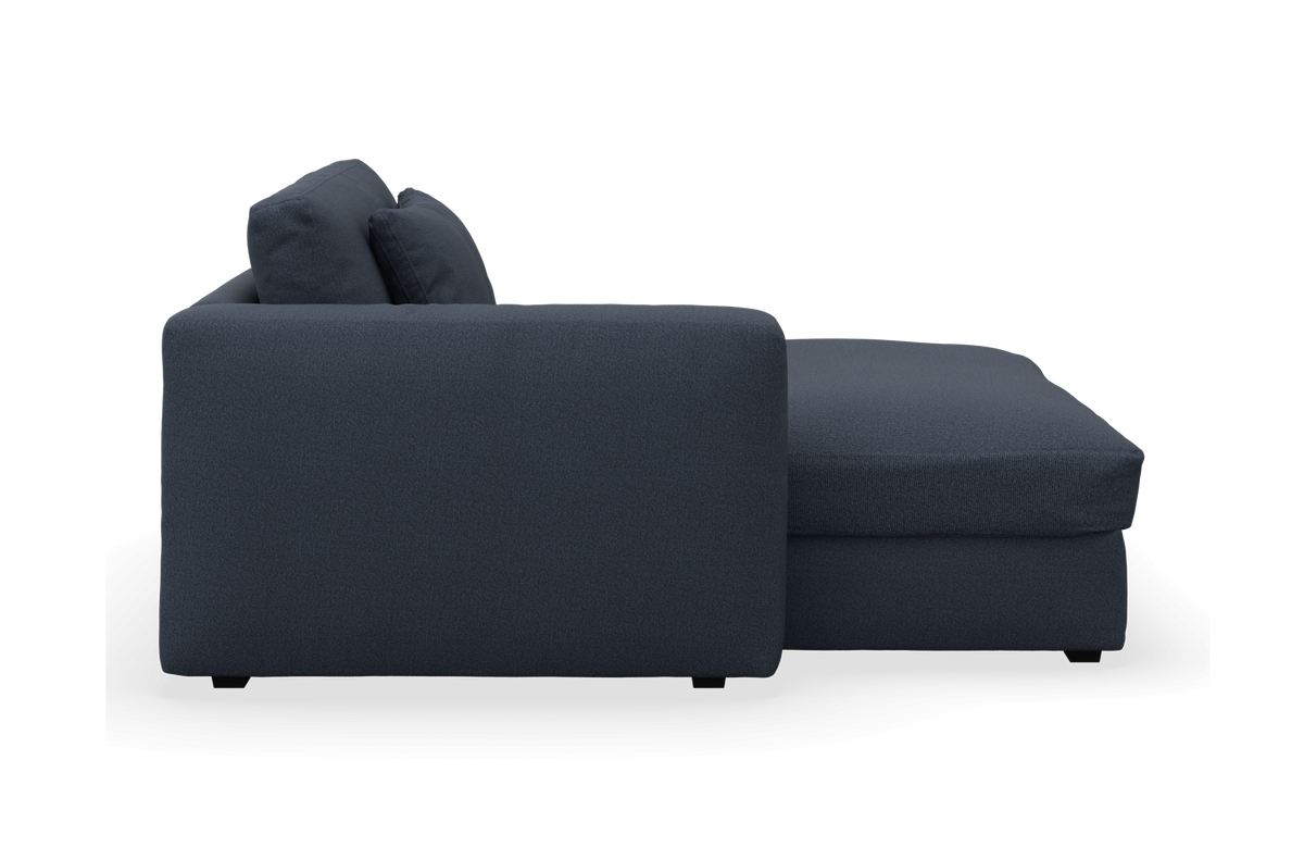 Mørkeblå sofa med chaiselong set fra siden på hvid baggrund.