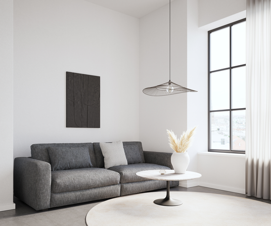 Lyst skandinavisk stuehjørne med grå sofa, rundt sofabord med marmorlook, hvid vase med pampasgræs, stort sort sprossevindue og let trådpende l.