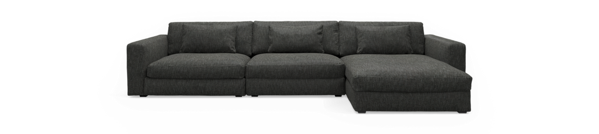 Mørkegrå hjørnesofa med chaiselong til højre, fotograferet lige for mod sort baggrund.