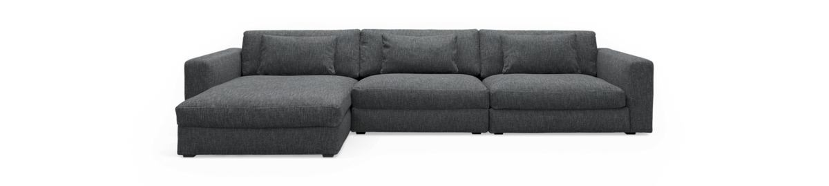 Mørkegrå hjørnesofa med chaiselong til venstre på sort baggrund.
