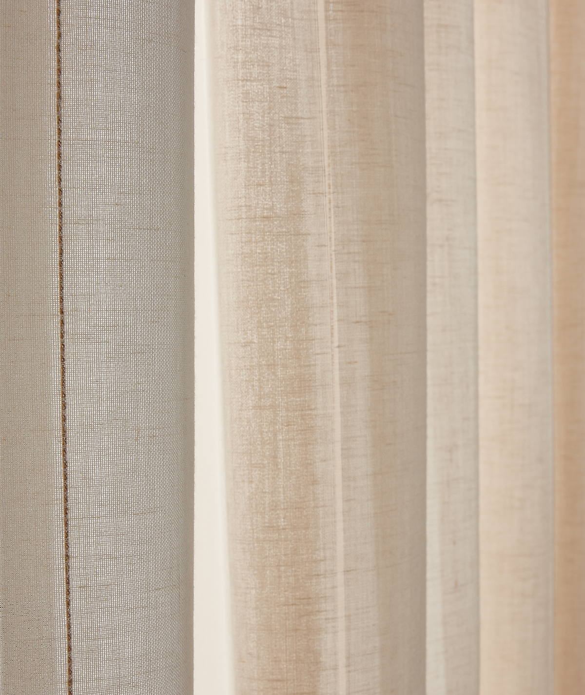 Nærbillede af lyse beige og hvide gardiner i linnedlook med bløde folder.
