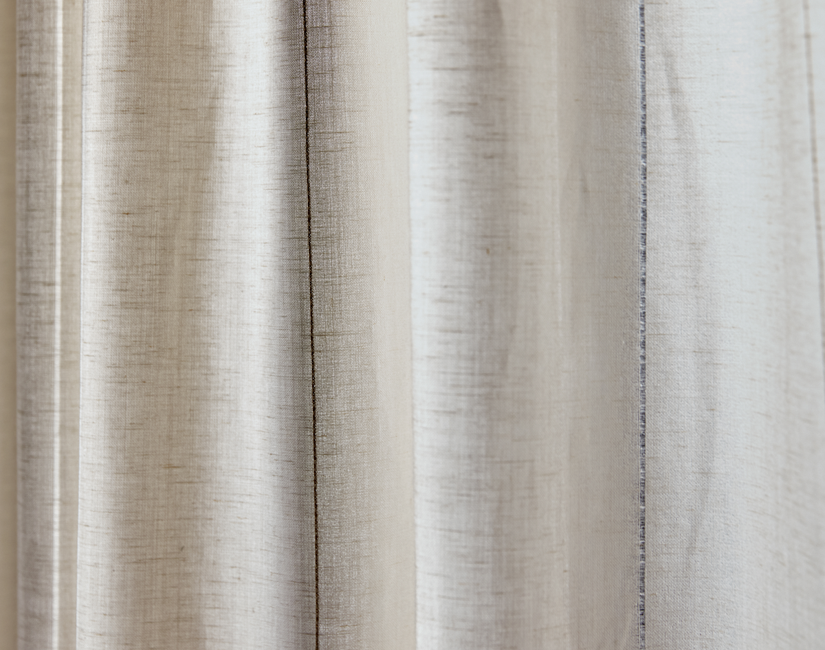 Nærbillede af beige gardin i hørlook med bløde folder i neutrale nuancer.