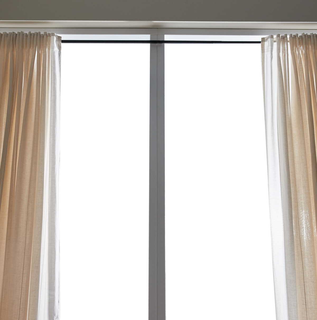 Lyse, transparente beige gardiner på en sort gardinstang, der indrammer et vindue i dagslys.