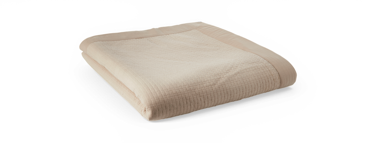 Sammenfoldet beige quiltet plaid/soverkast med bred kant på sort baggrund.