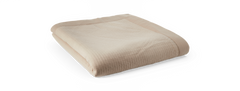 Sammenfoldet beige quiltet plaid/soverkast med bred kant på sort baggrund.