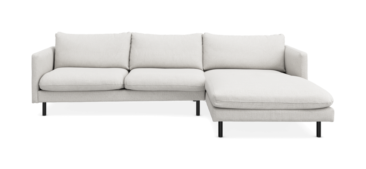 L‑formet sofa med højre chaiselong i lyst beige stof, slanke sorte ben, tre sædehynder og fire ryghynder.