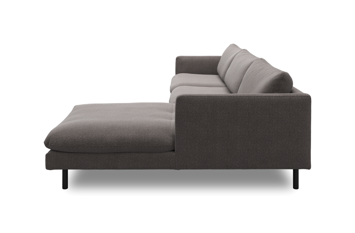Sideview af en grå stofsofa med venstrevendt chaiselong og sorte ben, frilagt på hvid baggrund.