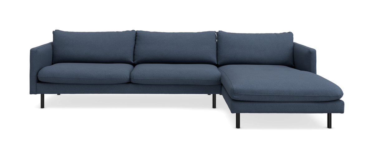 Blå L‑formet hjørnesofa med chaiselong til højre og slanke sorte ben, frontvisning i studie.
