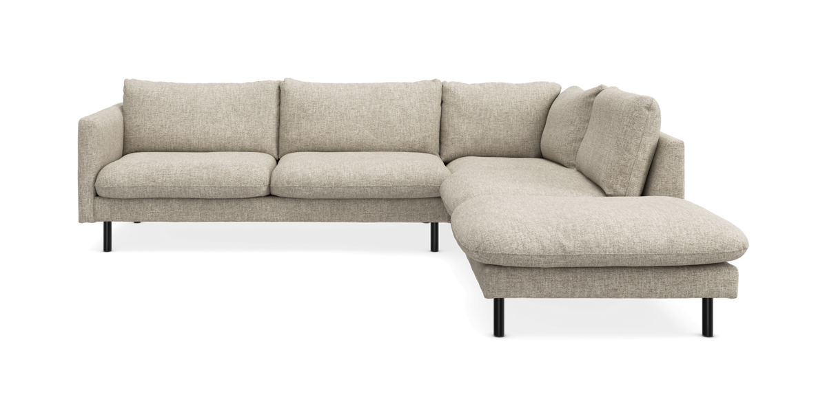 Beige L-formet modulsofa med chaiselong til højre og slanke sorte ben, frilagt på hvid baggrund.