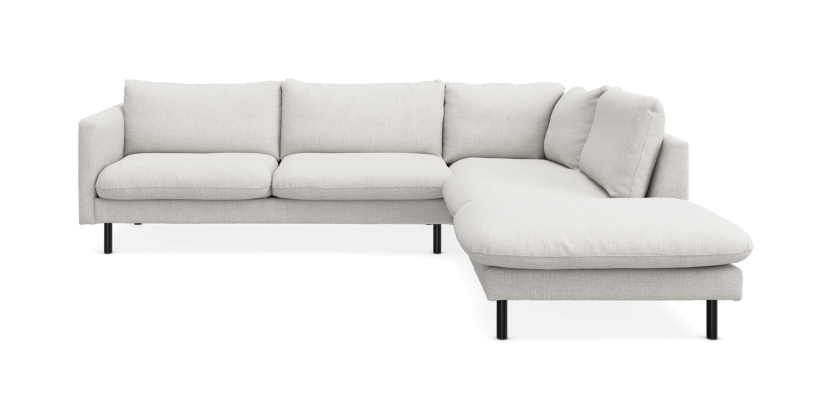 Lys beige L‑sofa med chaiselong til højre på sorte ben, frontvisning.