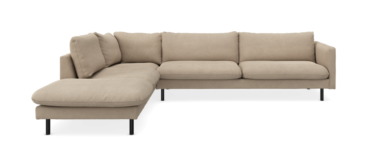 Beige L‑sofa med venstre chaiselong, slanke sorte ben og bløde puder – produktbillede på sort baggrund.