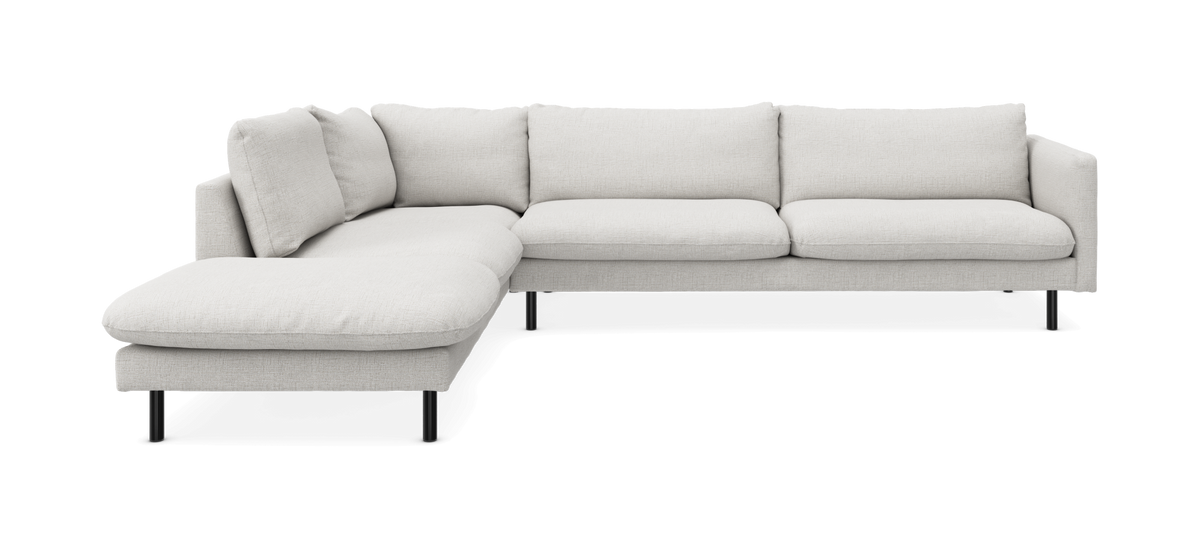 L‑formet lys beige modulsofa med venstre chaiselong og slanke sorte ben, frilagt på hvid baggrund.