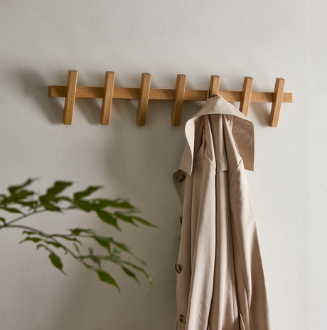Vægmonteret knagerække i eg med en beige trenchcoat i en lys, minimalistisk entré.