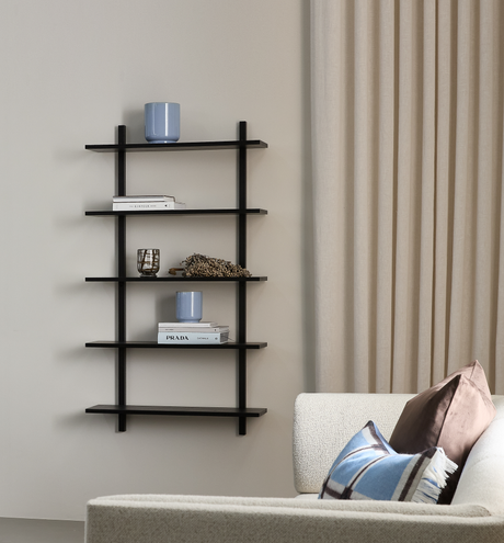 Lys stue med en sort væghylde med bøgerne ”KINFOLK” og ”PRADA OPTICAL”, en blå vase og et lille glas; beige gardiner og en cremefarvet sofa med puder.