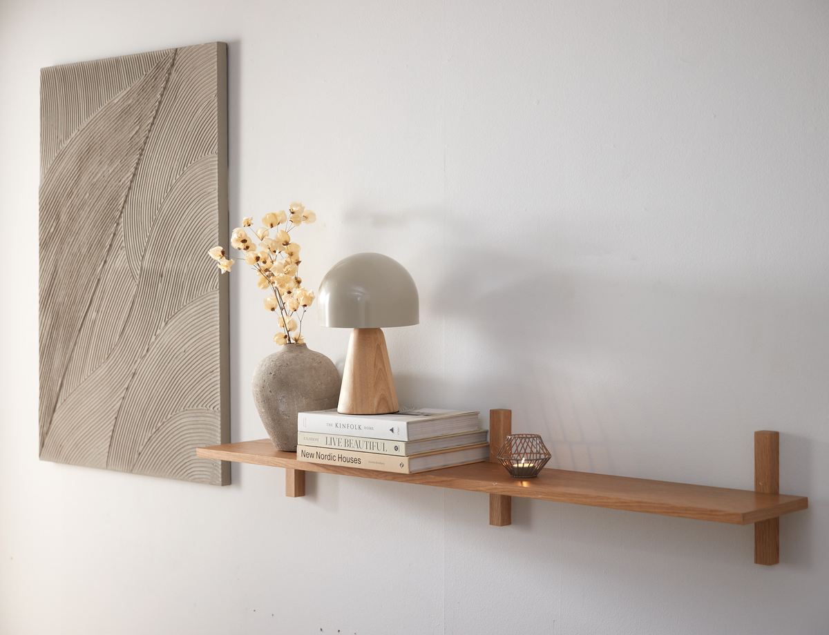 Væghylde i træ med bordlampe, vase med tørrede blomster, et fyrfadslys og tre bøger: The Kinfolk Home, Live Beautiful og New Nordic Houses.