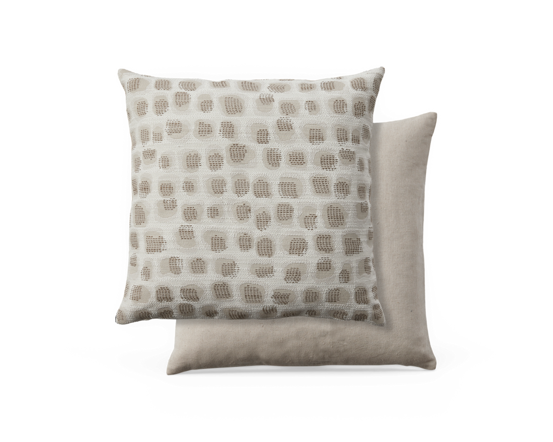 To beige pyntepuder; den forreste med hævet kvadratisk prikket mønster i taupe på creme, den bagerste i ensfarvet hørbeige.