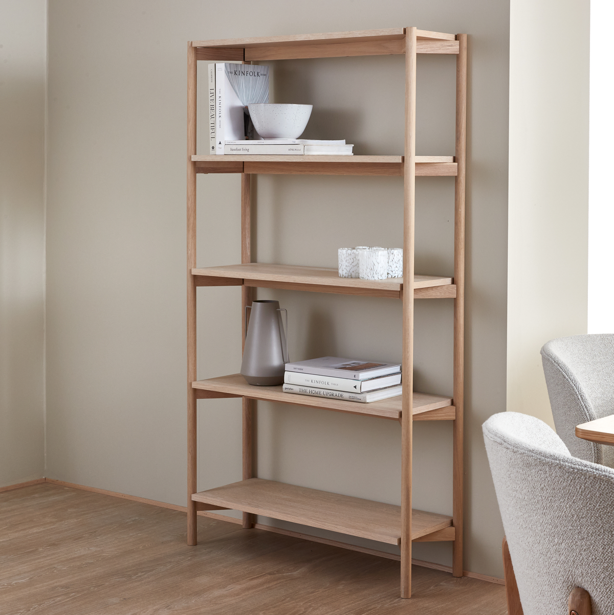 Åben reol i lys eg med bøger (Kinfolk, The Home Upgrade), skål, kande og lys i et lyst skandinavisk rum.