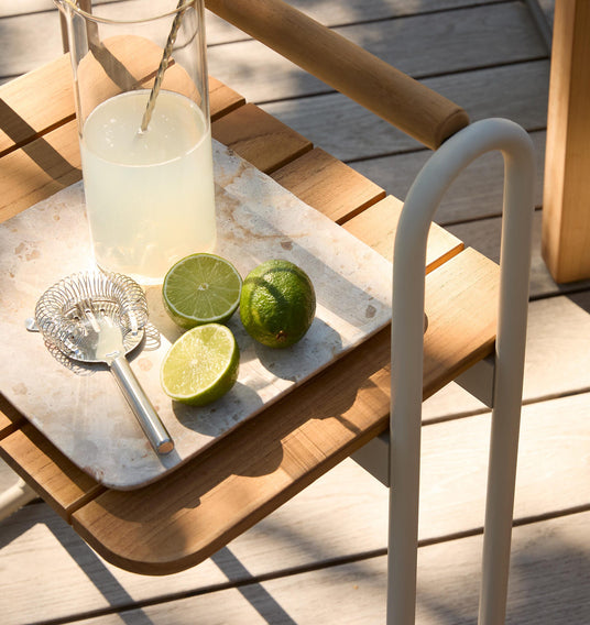 Nærbillede af marmorbakke på trævogn udendørs med en karaffel med limonade, halverede lime og en cocktailsigte i varmt sollys.