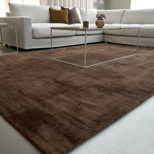 Brunt tæppe i stue med hvid hjørnesofa og minimalistisk sofabord i metal.