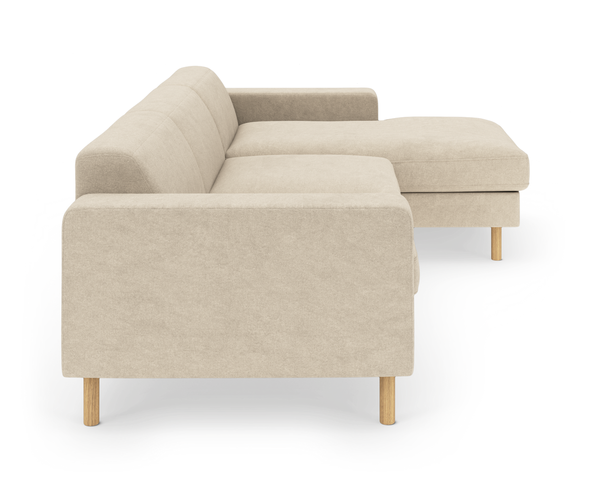 Beige L‑sofa med chaiselong til højre, lige armlæn og lyse træben, frilagt på hvid baggrund.