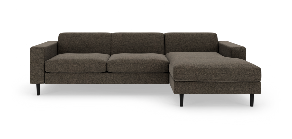 Modulsofa med chaiselong til højre i mørk brungråt stof og sorte ben, frilagt på hvid baggrund.