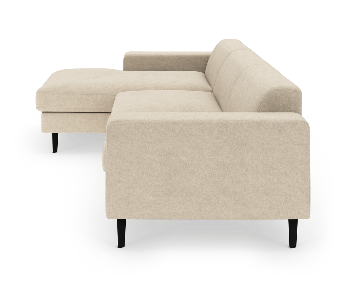 Beige L-formet modulsofa med chaiselong til venstre og sorte ben, set skråt forfra mod hvid baggrund.