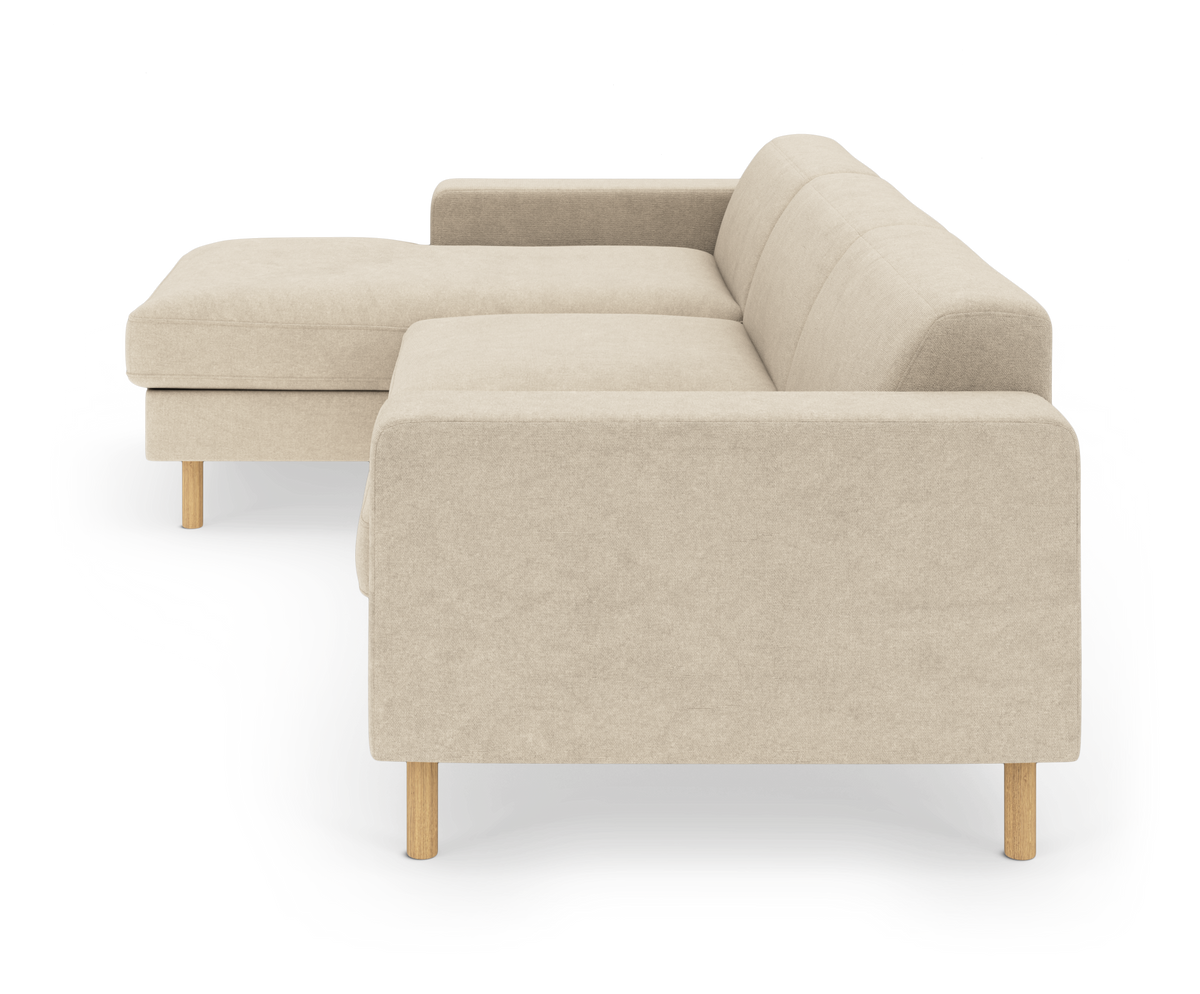 Beige L‑formet hjørnesofa med chaiselong og lyse træben, frilagt på hvid baggrund.