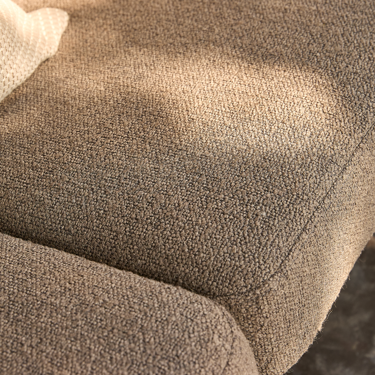 Nærbillede af beige bouclé-sofapude med sollys over teksturen og et lyst strikket plaid i hjørnet.