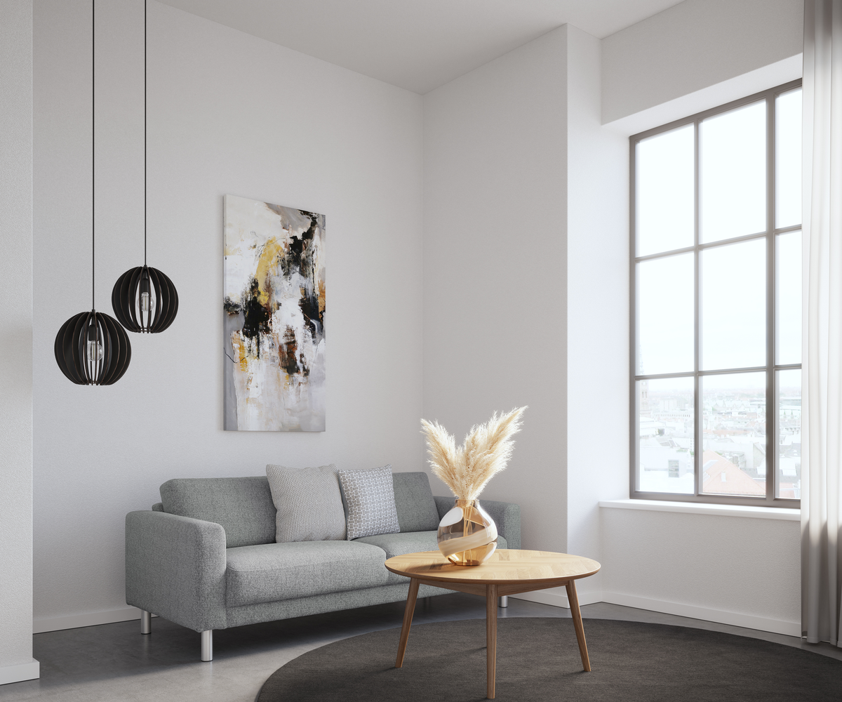 Lyst minimalistisk stue med grå sofa, abstrakt vægkunst, to sorte pendellamper og rundt sofabord i træ med vase med pampasgræs ved stort vindue med byudsigt.