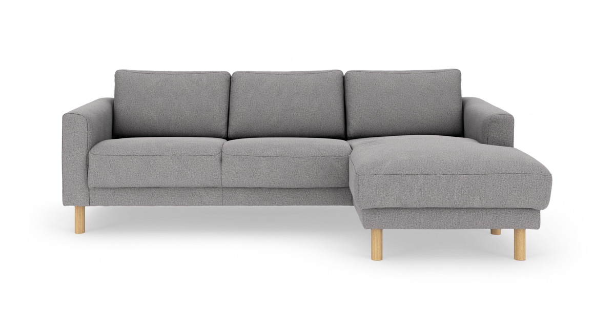 Grå hjørnesofa med chaiselong til højre og runde træben, frilagt på hvid baggrund.