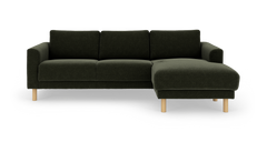Mørkegrøn tresæders sofa med chaiselong til højre og runde lyse træben, frilagt på hvid baggrund.