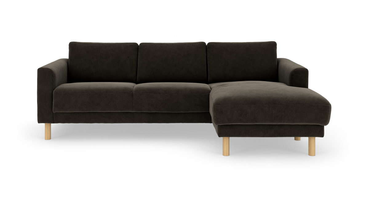 Mørkegrå hjørnesofa med chaiselong til højre og lyse træben, frilagt på hvid baggrund.