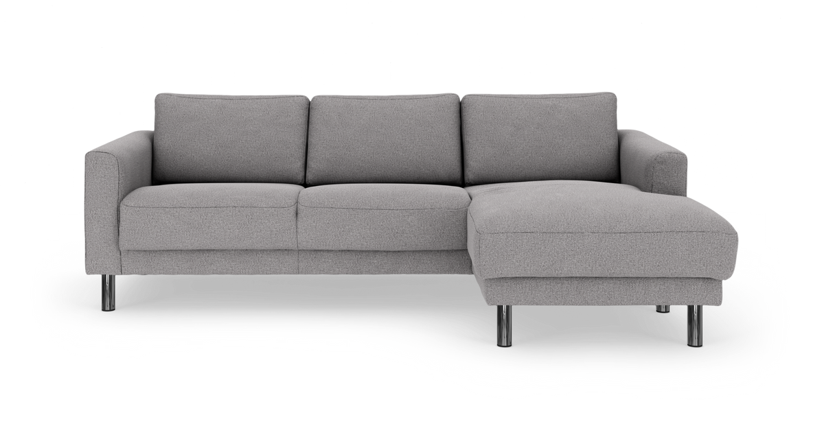 Grå hjørnesofa med chaiselong til højre og kromben, fotograferet forfra på hvid baggrund.