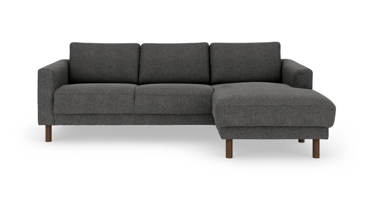 Mørkegrå hjørnesofa med chaiselong til højre og træben, set forfra mod hvid baggrund.