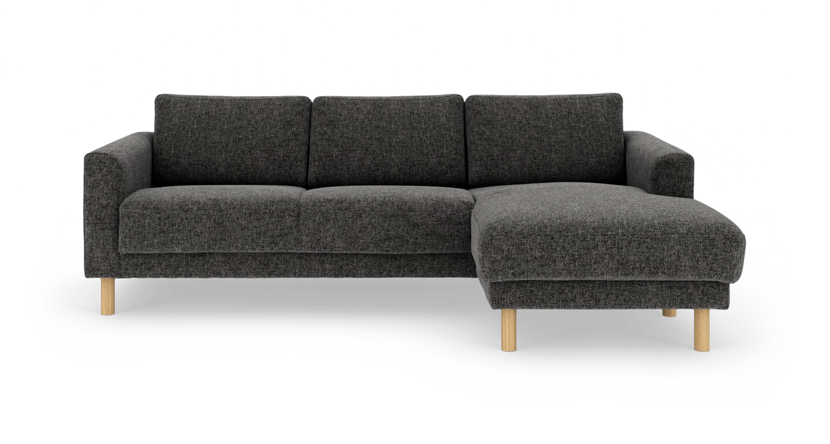 Mørkegrå hjørnesofa med chaiselong til højre og lyse træben, fritlagt på hvid baggrund.
